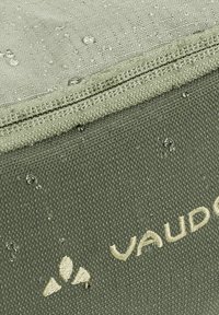 Tissu imperméable vert avec une surface texturée, présentant un logo beige et de petites gouttes d'eau sur le matériau.