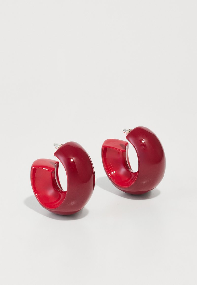 Červené akrylové náušnice v tvare kruhu s lesklým povrchom, ktoré majú zakrivený, otvorený dizajn a zapínanie na kolík. Tvar je okrúhly a masívny.