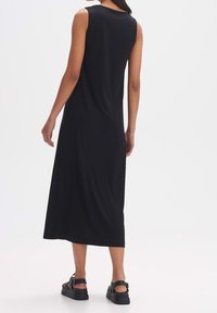 Robe maxi sans manches noire en tissu doux avec une coupe décontractée, dotée d'un col rond et d'une texture lisse, portée avec des sandales épaisses.