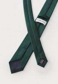 Donkergroene stropdas met diagonale ribbelstructuur, met een marineblauwe punt en een wit label met "PIER ONE" aan de achterkant.