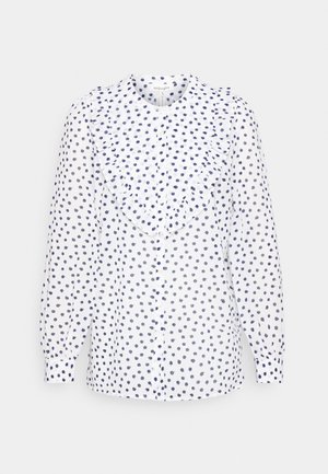 Blusa longa de mangas brancas com bolinhas azuis marinho, apresentando um detalhe franzido na parte da frente e fecho com botões. Feita de material leve e transparente.