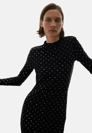Vestido negro de manga larga hecho de una tela suave, que presenta adornos circulares plateados dispuestos en un patrón de puntos por toda la superficie.