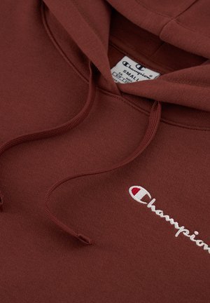 Braune Kapuzenjacke aus Baumwolle, mit einer Fronttasche, Kordeln und einem in Weiß gestickten Champion-Logo. Glatte Textur.