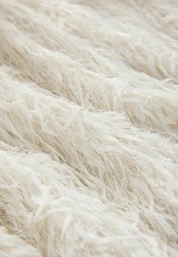 Struktureret stof med lange, fine hvide fibre og subtile metaltråde for glimt; blød og fluffy udseende.