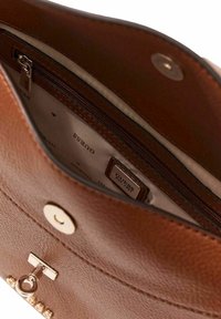 Intérieur de sac à main en cuir marron, comprenant une poche zippée, une étiquette de marque et des accents de quincaillerie dorée. Finition douce et texturée.