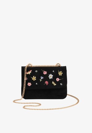 Bolso cruzado de ante negro con correa de cadena dorada, que presenta un bordado colorido de flores y mariposas en la parte frontal. Forma rectangular compacta.