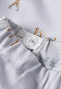 Lichtgrijze stof met dierpatronen heeft een knoopsluiting, elastische tailleband en een zachte textuur. Zichtbare steken en details accentueren het geheel.