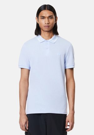 Camisa polo azul claro con collar clásico, mangas cortas y un pequeño logo bordado en el pecho. Textura de tejido suave y lisa.