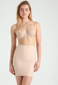 Sutiã acolchoado bege com alças ajustáveis, combinado com uma saia slip justa, sem costuras, de comprimento médio até a coxa, na mesma tonalidade. Textura suave.