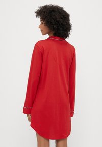 Rochie roșie cu mânecă lungă, guler, tiv curbat și cusături decorative pe manșete. Material moale, ușor, cu textură netedă.