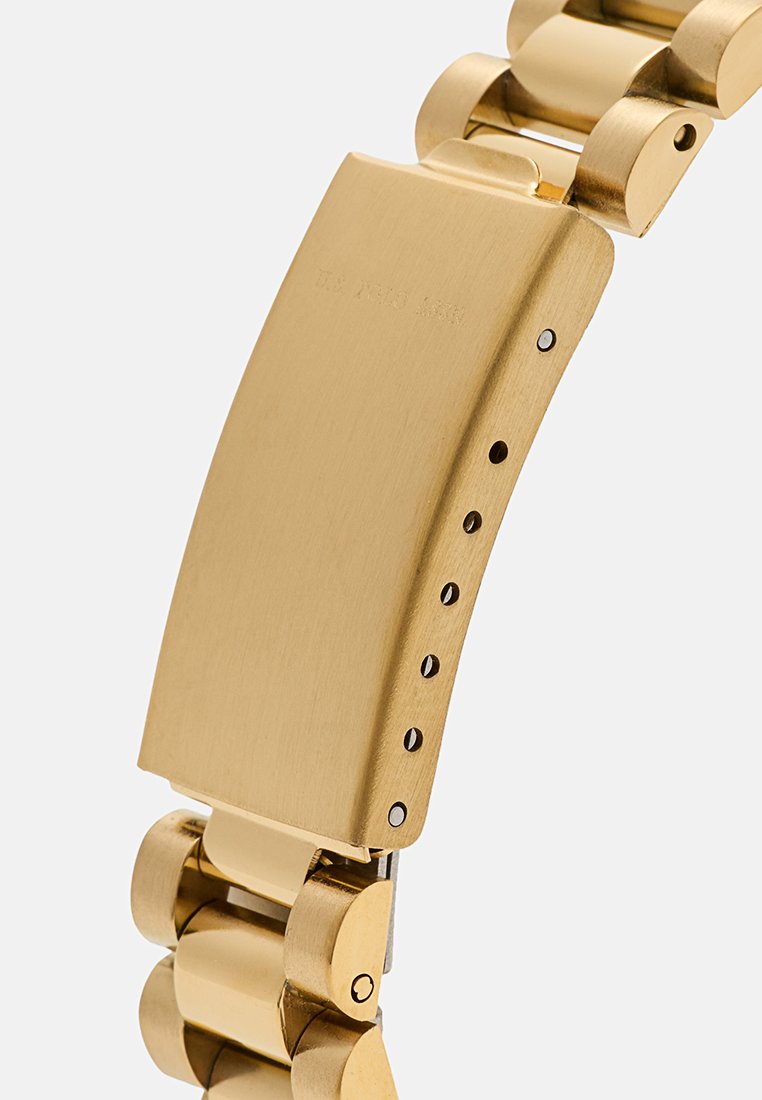 Montre-bracelet en métal doré avec une finition brossée, dotée d'un large boîtier rectangulaire, de maillons arrondis et de trous d'ajustement le long du bracelet.