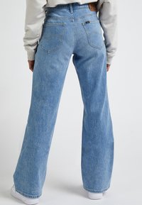 Ljusblå vida jeans i denim med hög midja, två bakfickor och en logotyp-patch i läder på midjebandet.