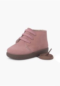 Botín de ante rosa con tres agujeros para lazada y suela de goma marrón, con punta redondeada y un cordón marrón a juego al lado del zapato.