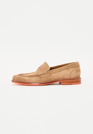 Suède loafers in lichtbruin met ton-sur-ton stiksel, voorzien van decoratieve gouden studs langs de kraag en een houten hak.