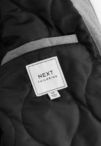 Captuse interioare negre, cusute, cu accente gri. Eticheta spune "NEXT TAILORING," include un label cu dimensiunea și este fabricat în China.