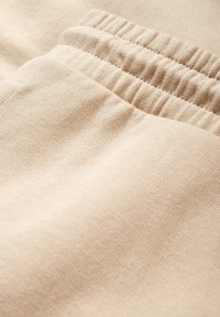 Beżowe dresowe spodnie bawełniane z prążkowanym paskiem i fakturowaną tkaniną. Charakteryzują się gładkim wykończeniem i subtelnymi detalami szwów.