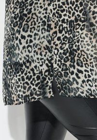 Blusa a stampa leopardata in tessuto leggero e trasparente, con motivi neri e beige, orlo spaccato e vestibilità ampia, abbinata a leggings neri.