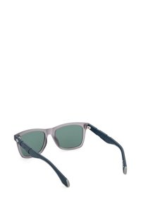 Occhiali da sole con una montatura grigia traslucida, lenti verdi e stanghette blu navy. Presentano dettagli metallici e un design elegante e angolare.