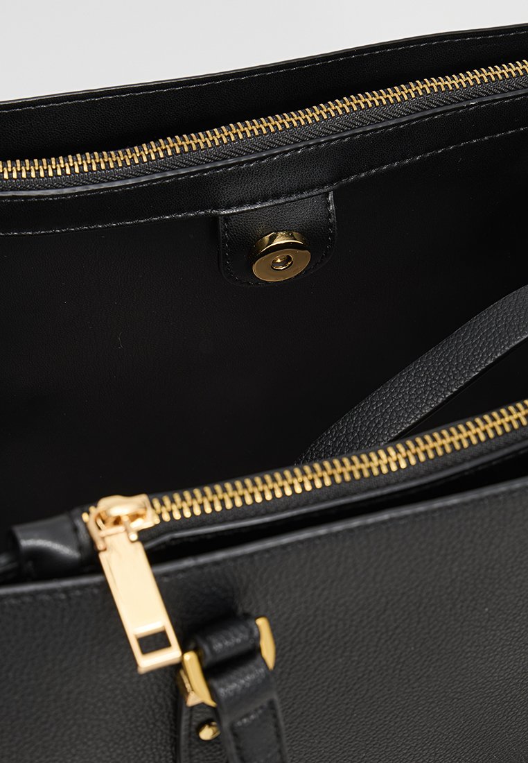 Interno di una borsa a tracolla nera in pelle con una cerniera dorata, una chiusura a scatto magnetico e fodera testurizzata. Presenta spallacci robusti e dettagli metallici.