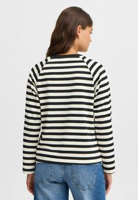 Black and white striped long-sleeve shirt with a rounded neckline and raglan sleeves, paired with blue denim jeans.