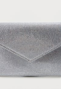 Stříbrná obálková kabelka pokrytá malými odrazovými kamínky na jednobarevném bílém pozadí.