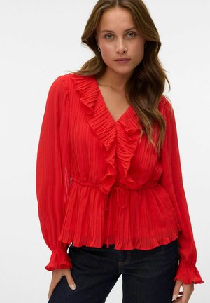Blouse plissée rouge avec des détails en volants le long de l'encolure et des manches, dotée d'une taille nouée et de longues manches fluides.