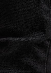 Svart denimtyg med en slät textur, som uppvisar en lätt stretch och ett subtilt vävningsmönster, med veck och rynkor.