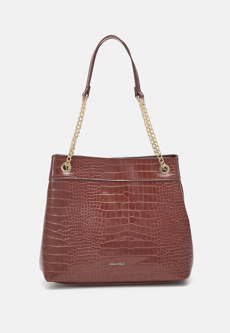 Sac à main marron en cuir synthétique imitation crocodile avec des bandes en chaîne dorée et le logo "Anna Field" à l'avant, sur un fond neutre.