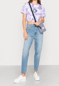 Fialový crop top s batikou ve tvaru kruhu, světle modré rovné džíny a bílé platformové tenisky. Malá šedá crossbody kabelka.