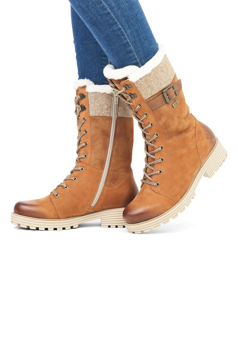 Botas de cuero marrón claro con cordones, un cuello esponjoso de crema, tejido gris texturizado y un cierre lateral; acentuadas con herrajes metálicos y suelas gruesas.