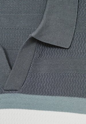Grijze stofstructuur met een v-hals kraag, voorzien van zigzagpatronen en een gelaagd ontwerp. Inclusief een lichter blauw-grijze accent aan de onderkant.