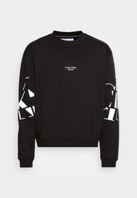 Černá mikina s dlouhými rukávy, kulatým límcem a bílým logem Calvin Klein Jeans na hrudi. Geometrický bílý vzor na rukávech.