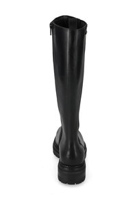 Stivale alto in pelle nera con suola chunky, zip posteriore e tirante, mostrato da dietro su uno sfondo bianco.