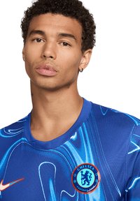Blauw Chelsea FC-shirt met een golvend design en Nike-logo. Het ronde clubembleem is prominent op de borst geplaatst, met een textuur in de stof.