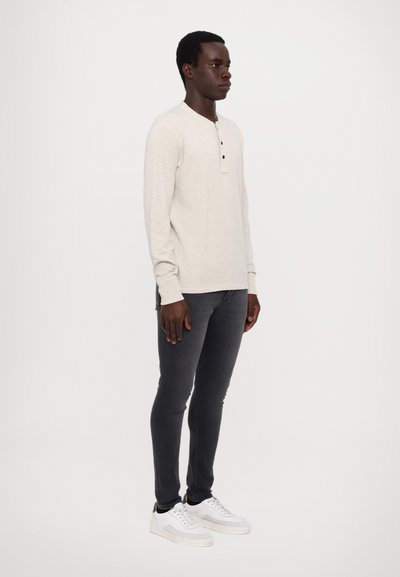 Lys beige langermet skjorte med tre knapper ved halsen, kombinert med mørk grå skinny jeans og hvite sneakers.