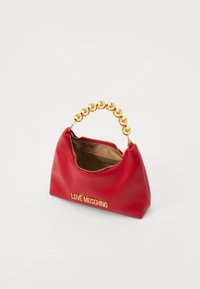 Red faux leather handbag with a golden bead handle and gold logo. Features a zip closure and a single beige interior pocket. Compact shape.