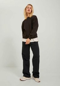 Hanorac negru cu manșete și tiv cu striații, purtat peste un top deschis la culoare. Asortat cu pantaloni negri lejeri și adidași deschiși la culoare.