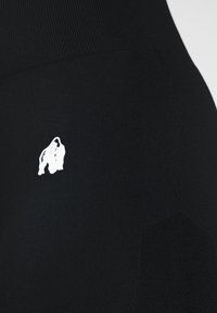 Black leggings featuring a textured fabric, high waistband, and a small white logo accent on the side. Smooth, stretchy material.