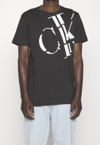 Svart bomulls-t-shirt med djärva vita grafiska bokstäver, en avslappnad passform och korta ärmar, med en något rundad halsringning och ren fåll.