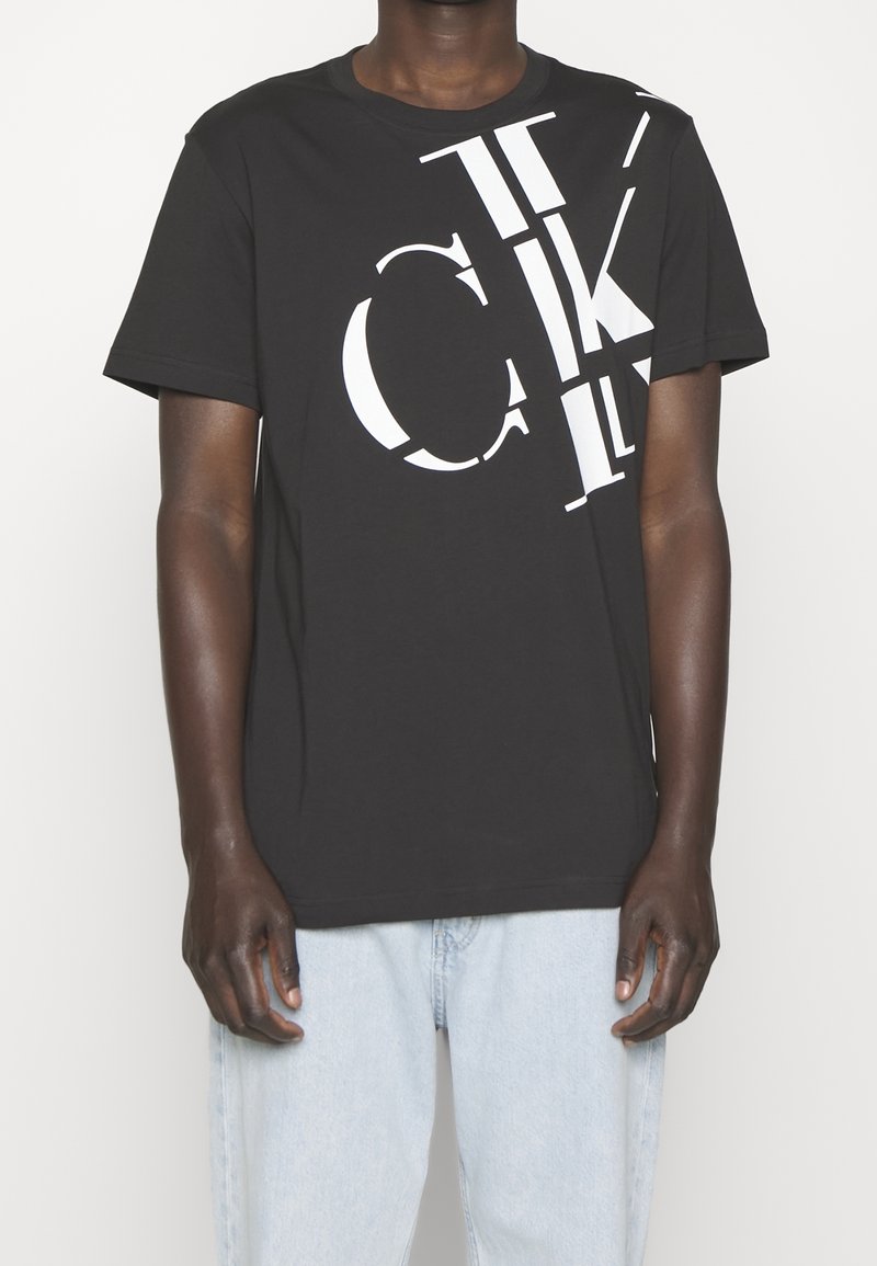 Svart bomulls-t-shirt med djärva vita grafiska bokstäver, en avslappnad passform och korta ärmar, med en något rundad halsringning och ren fåll.