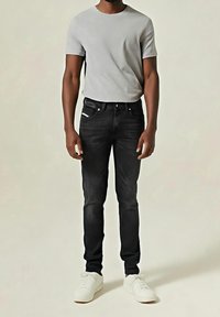 Grå t-shirt med kort ärm kombinerat med svarta slim-fit jeans. Jeans har framfickor och ett subtilt mönster, kompletterat med vita sneakers.