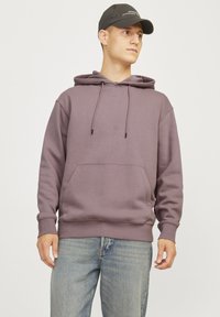 Sweatshirt in muted purple, featuring a hood, drawstrings, and front pocket. The fabric appears soft with a relaxed fit. Paired with blue jeans.