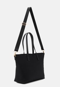 Black tote bag featuring dual top handles, a detachable adjustable strap, and gold-tone hardware. Made of a smooth fabric with no visible patterns.