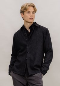 Mørkegrå ullskjorte med spiss krage, knappelukking foran og en lett teksturert overflate, kombinert med matchende grå bukser.