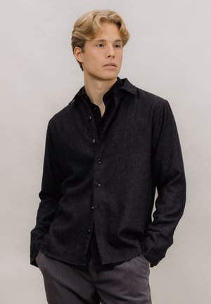 Mørkegrå ullskjorte med spiss krage, knappelukking foran og en lett teksturert overflate, kombinert med matchende grå bukser.