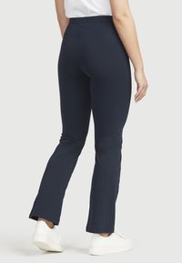 Navyblau elastische Taillenbundhose, figurnah an der Hüfte und am Saum ausgestellt. Glatte Textur mit weichem Finish, kombiniert mit weißen Sneakers.