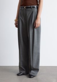 Gray pleated trousers with a tailored fit, made from woven fabric. Paired with a black belt featuring a gold buckle and black pointed shoes.