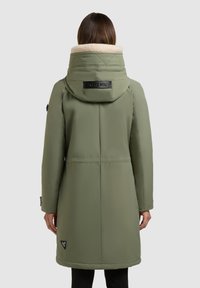 Olivovo zelený vypchávkovaný kabát s umelým ovčím golierom, prešívanými detailmi na kapucni a logom na dolnej strane. Dlhý, rovný strih.