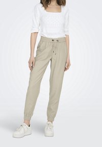 Beige joggerbroeken met een trekkoord in de taille en elastische boorden, gecombineerd met een gestructureerde witte top met vierkante hals en witte sneakers.