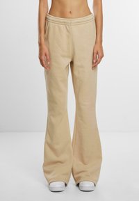 Lichtbeige sweatpants met een uitlopende pijp, elastische tailleband en zachte textuur, gecombineerd met witte sneakers.